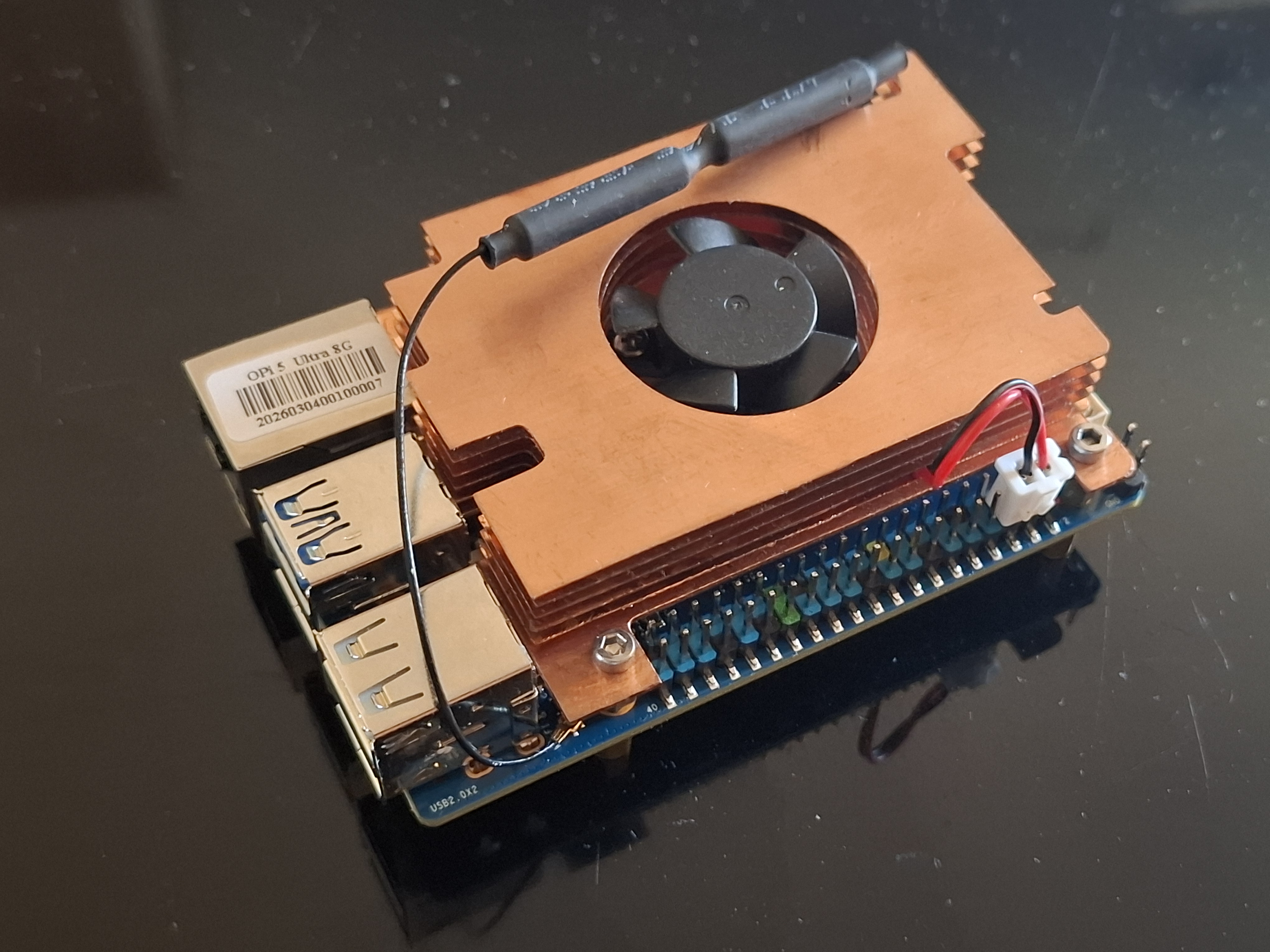 Fotografie jednodeskového počítače Orange Pi 5 Ultra s měděným chladičem a ventilátorem.