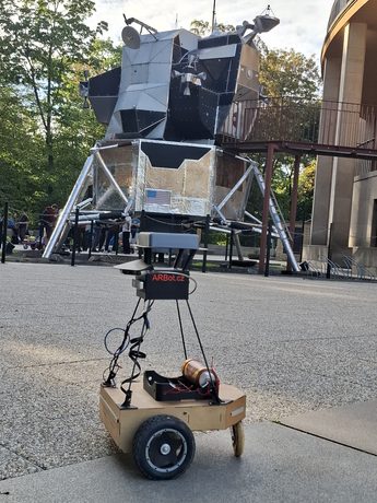 Robot ARBot verze PI na dlažbě před modelem lunárního modulu u Planetária v pražské Stromovce.